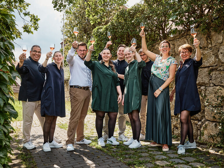 Eine Teil des Teams steht lachend und Weingläser hebend vor einer Mauer in der Oberpfalz